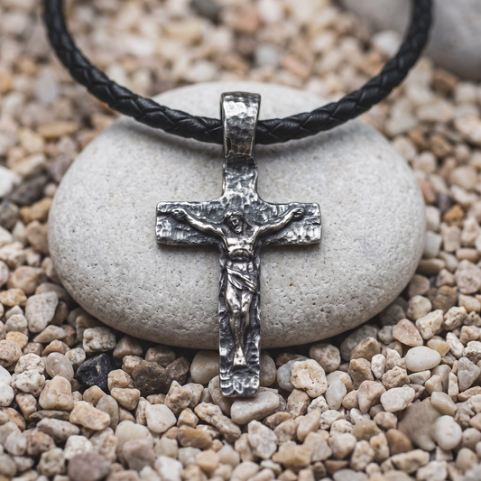 The Sixth Hour necklace in .999 fine silver — a rough-worked cross with a small figure standing out from the face, on a black braided leather cord