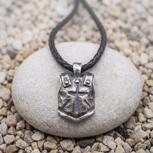The Breastplate necklace in .999 fine silver — a hammered breastplate with a cross cut into the face and three rivets across the chest, on a black braided leather cord
