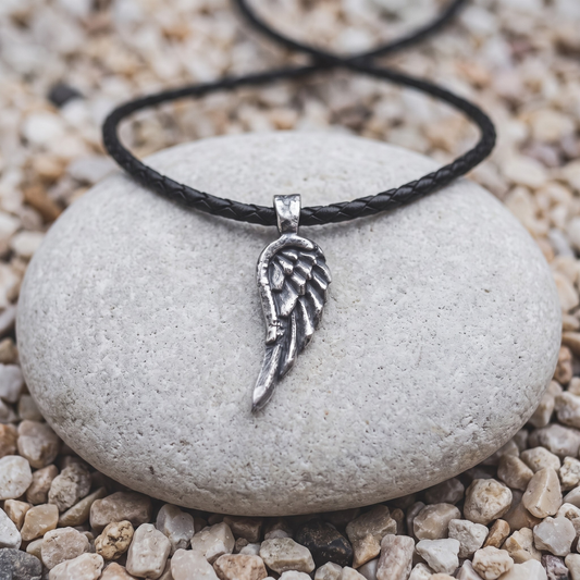 The Covering necklace in .999 fine silver — a single angel wing, oxidized deep between the feathers, on a black braided leather cord